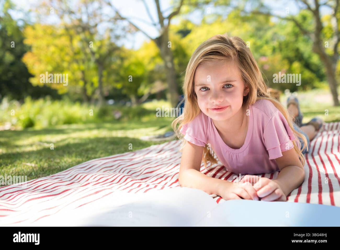 Fille enfant lisant livre ouvert sur couverture rayée rouge et blanche au parc herbeux, espace de copie Banque D'Images
