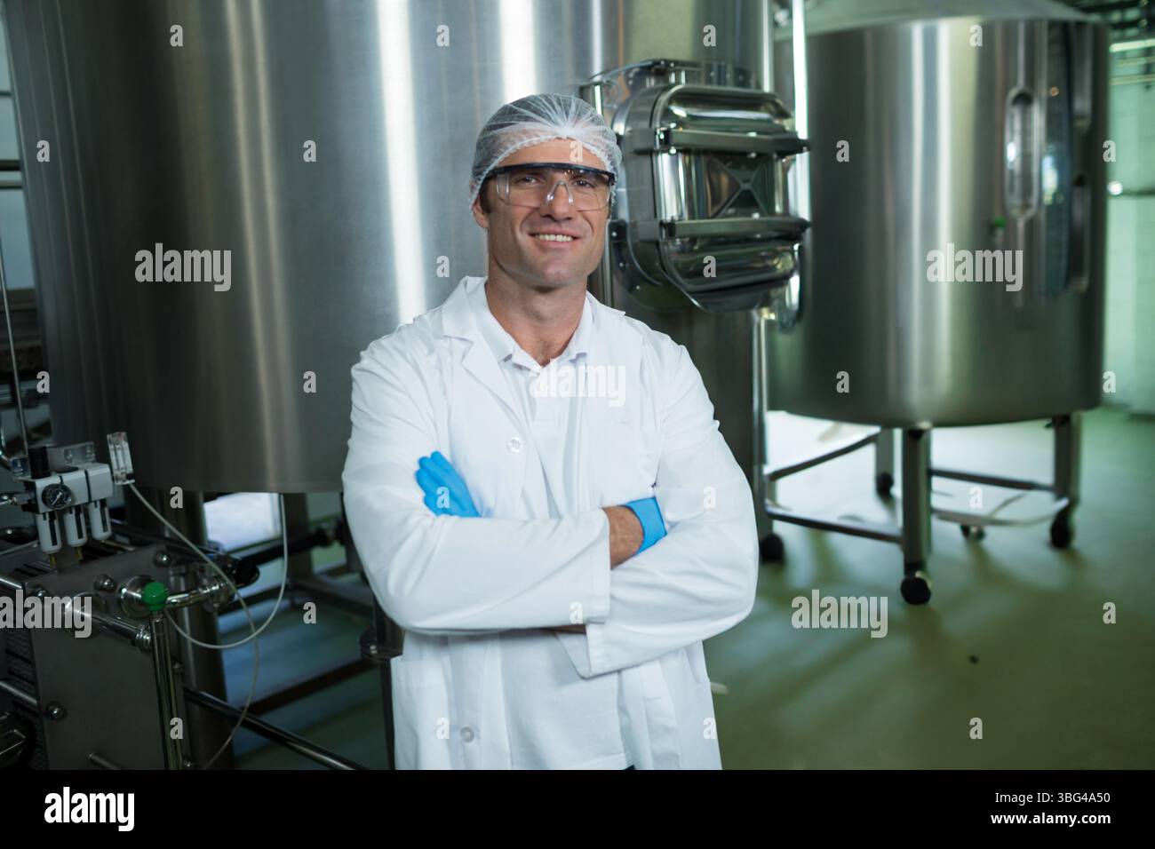 Homme inspectant les réservoirs en acier inoxydable dans l'usine de transformation des aliments tout en portant des lunettes de protection des gants en résille Banque D'Images