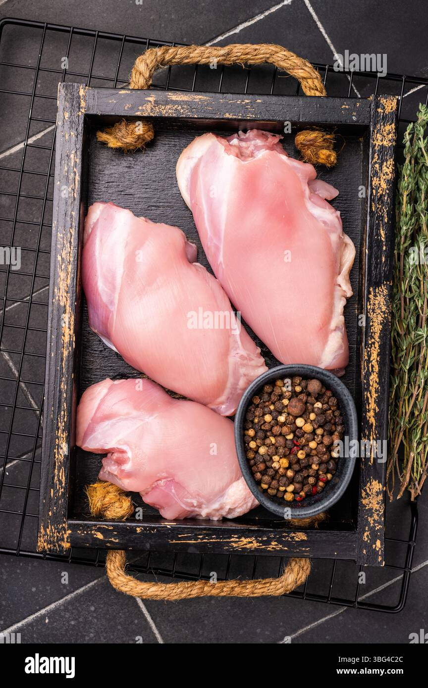 Filets de cuisses de poulet crus dans un plateau en bois. Fond noir. vue de dessus. Banque D'Images