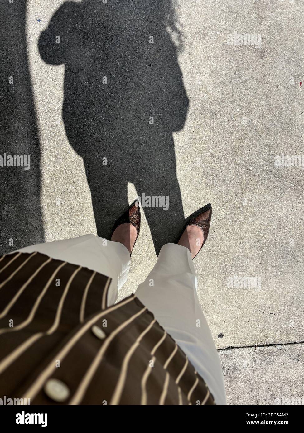 Silhouette de l'ombre d'une femme debout sur le trottoir en chemise rayée, pantalon ivoire et chaussures à bout pointu. Concept de mode et de style. Banque D'Images