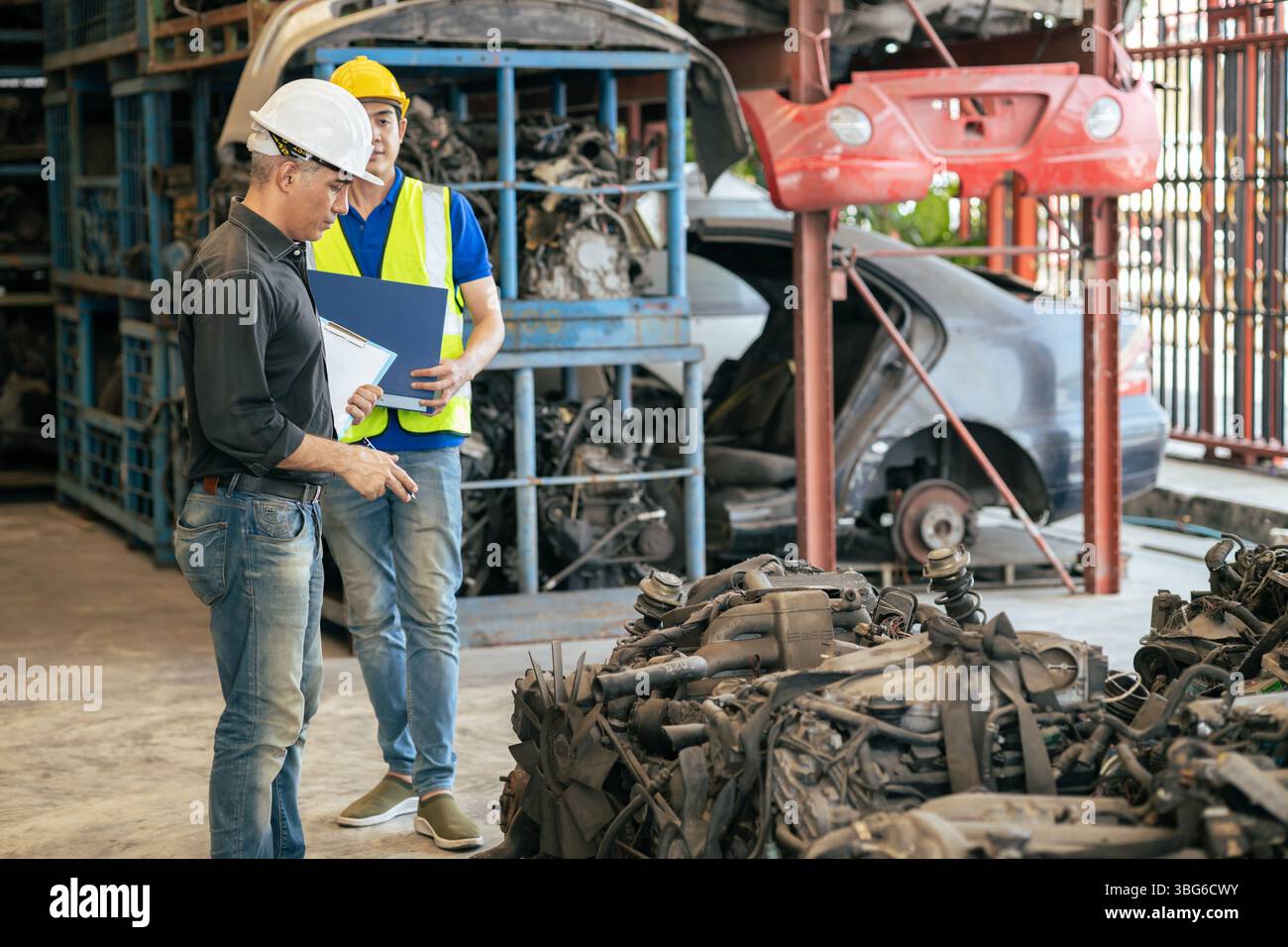 le propriétaire d'affaires de pièces de voiture d'occasion travaillant vérifier l'ordre de stock avec le jeune homme de technicien dans l'entrepôt de centre de pièces de rechange de véhicule d'occasion Banque D'Images
