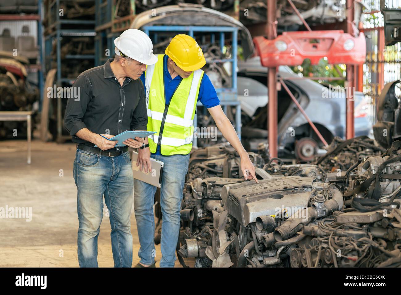 le propriétaire d'affaires de pièces de voiture d'occasion travaillant vérifier l'ordre de stock avec le jeune homme de technicien dans l'entrepôt de centre de pièces de rechange de véhicule d'occasion Banque D'Images