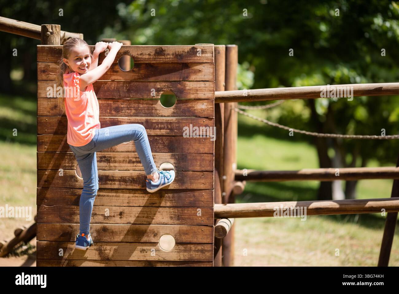 Fille enfant grimpant le mur de jeu en bois en utilisant des prises circulaires et un pont de corde au parc, espace de copie Banque D'Images