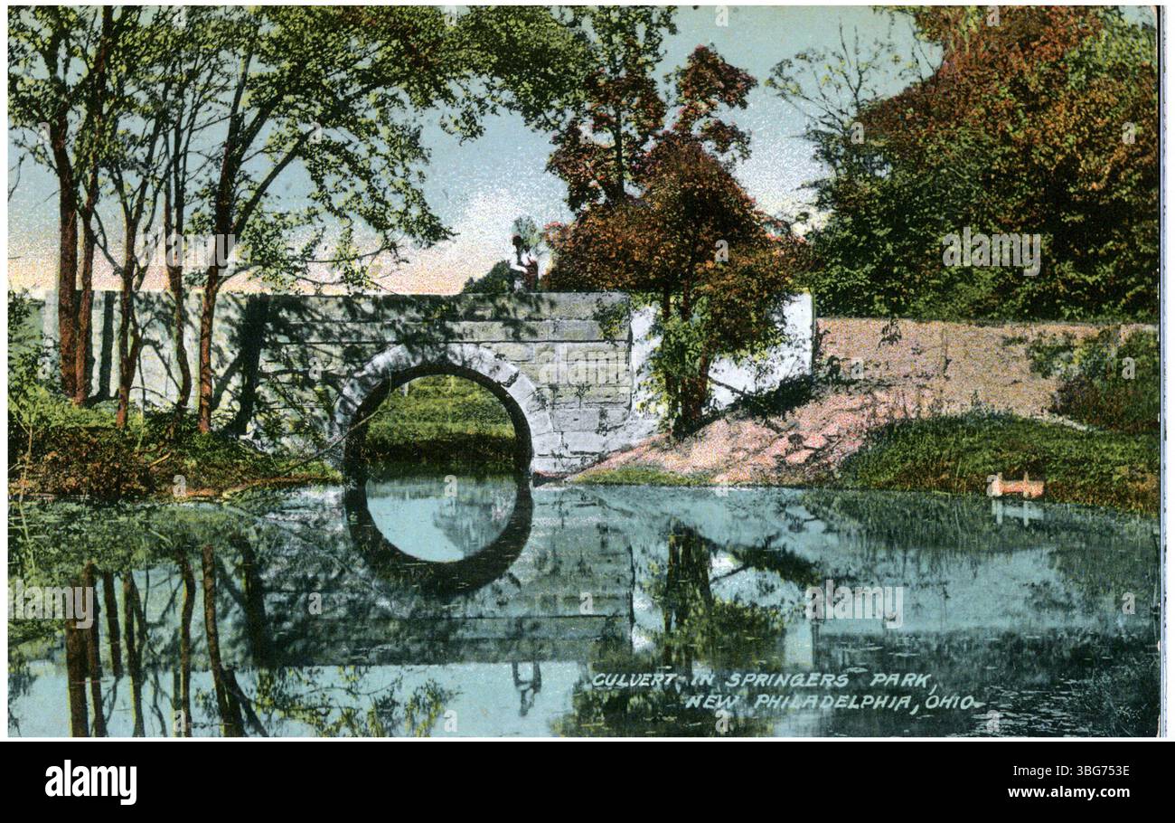Une photographie en couleur de 1911 d'un ponceau ou d'un pont en pierre à Springers Park, New Philadelphia, Ohio, enjambant un étang avec un beau reflet du pont dans l'eau. Banque D'Images