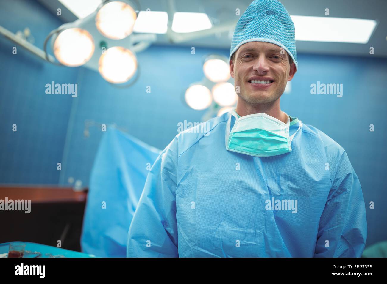 Chirurgien masculin en gommages bleus debout sous les lumières chirurgicales dans la salle d'opération, espace copie Banque D'Images