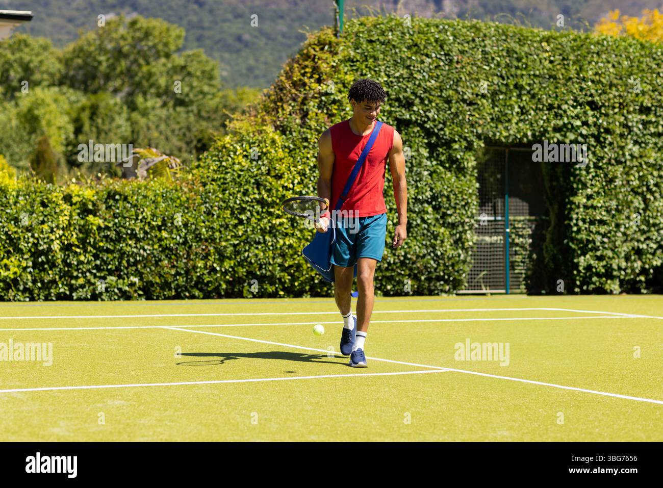 Homme afro-américain se promenant sur un court de tennis portant une raquette, un sac de sport et des balles de tennis Banque D'Images