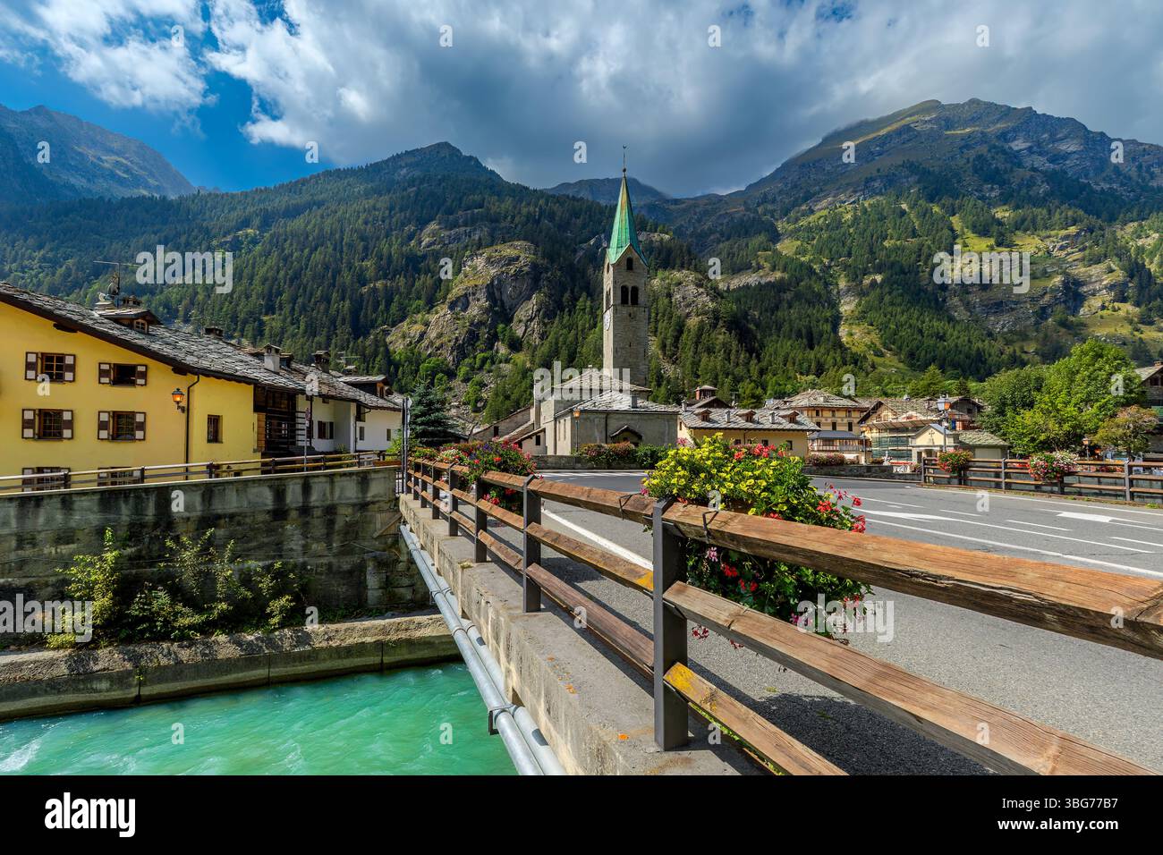 Un clocher d'église parmi les maisons en pierre sur fond de montagnes verdoyantes sous un ciel bleu nuageux à Gressoney Saint Jean, Italie. Banque D'Images