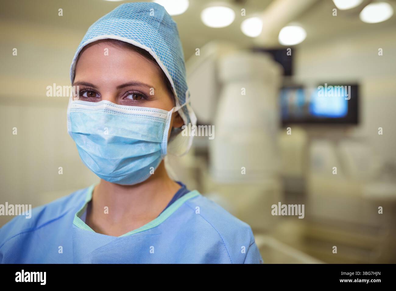 Chirurgien féminin debout dans la salle d'opération portant une combinaison de gommage, un masque et une casquette avec dispositif d'imagerie Banque D'Images