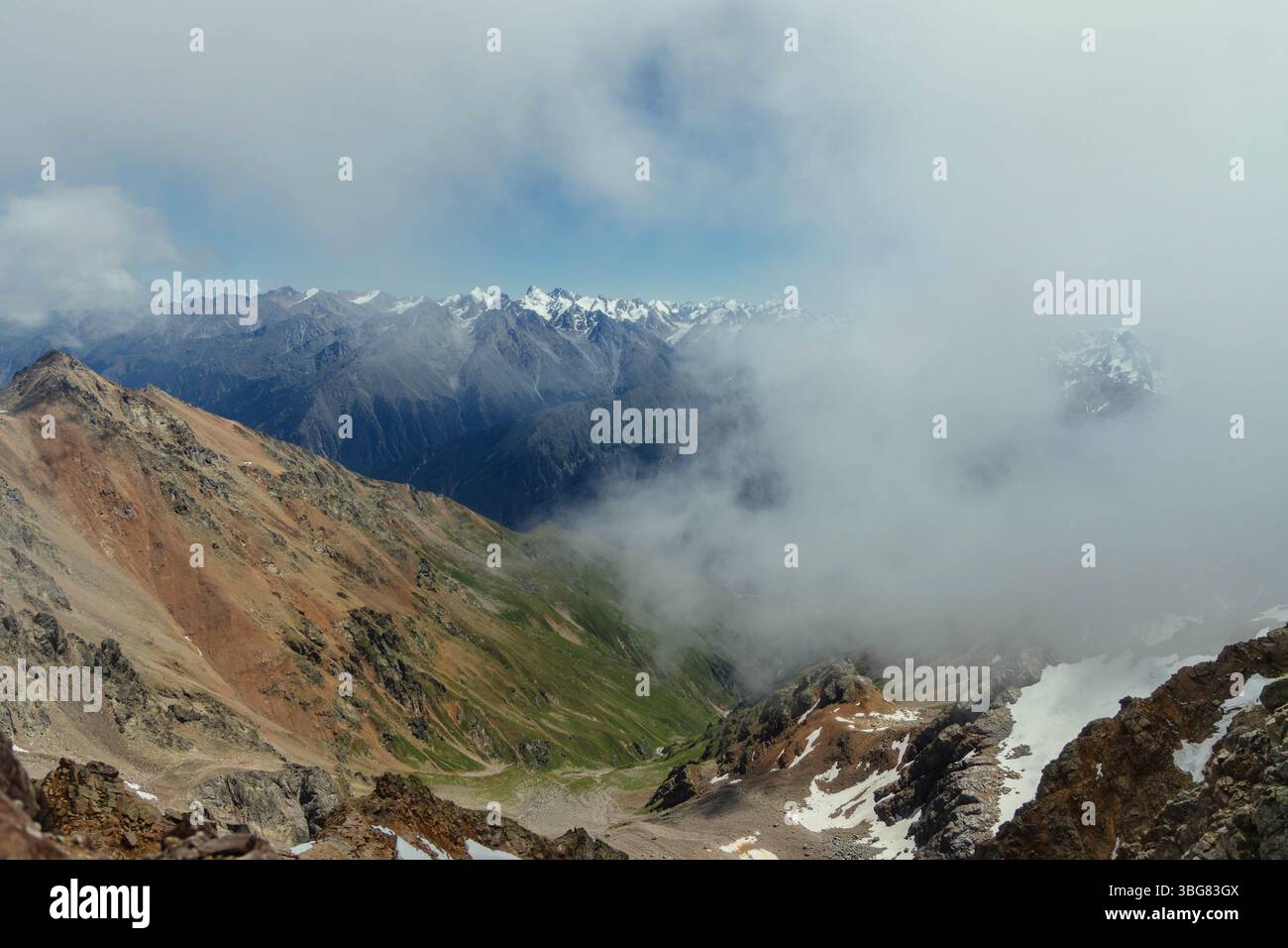 Les nuages dérivent à travers le paysage montagneux accidenté, révélant des sommets époustouflants et des vallées profondes sous le ciel bleu. la vue captivante met en valeur les majors de la nature Banque D'Images