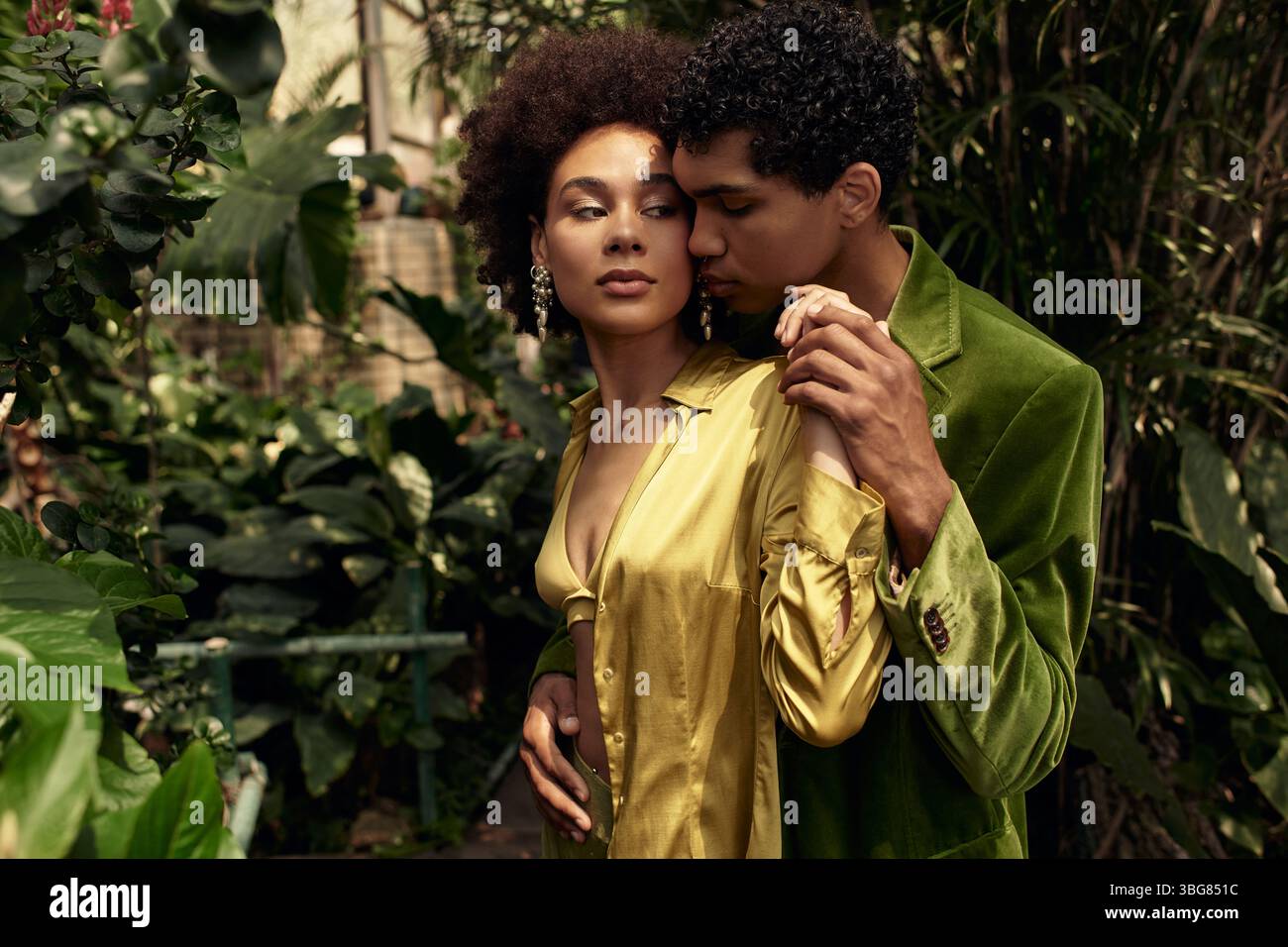 Un jeune couple partage un moment tendre entouré de verdure riche dans une serre cosy. Banque D'Images