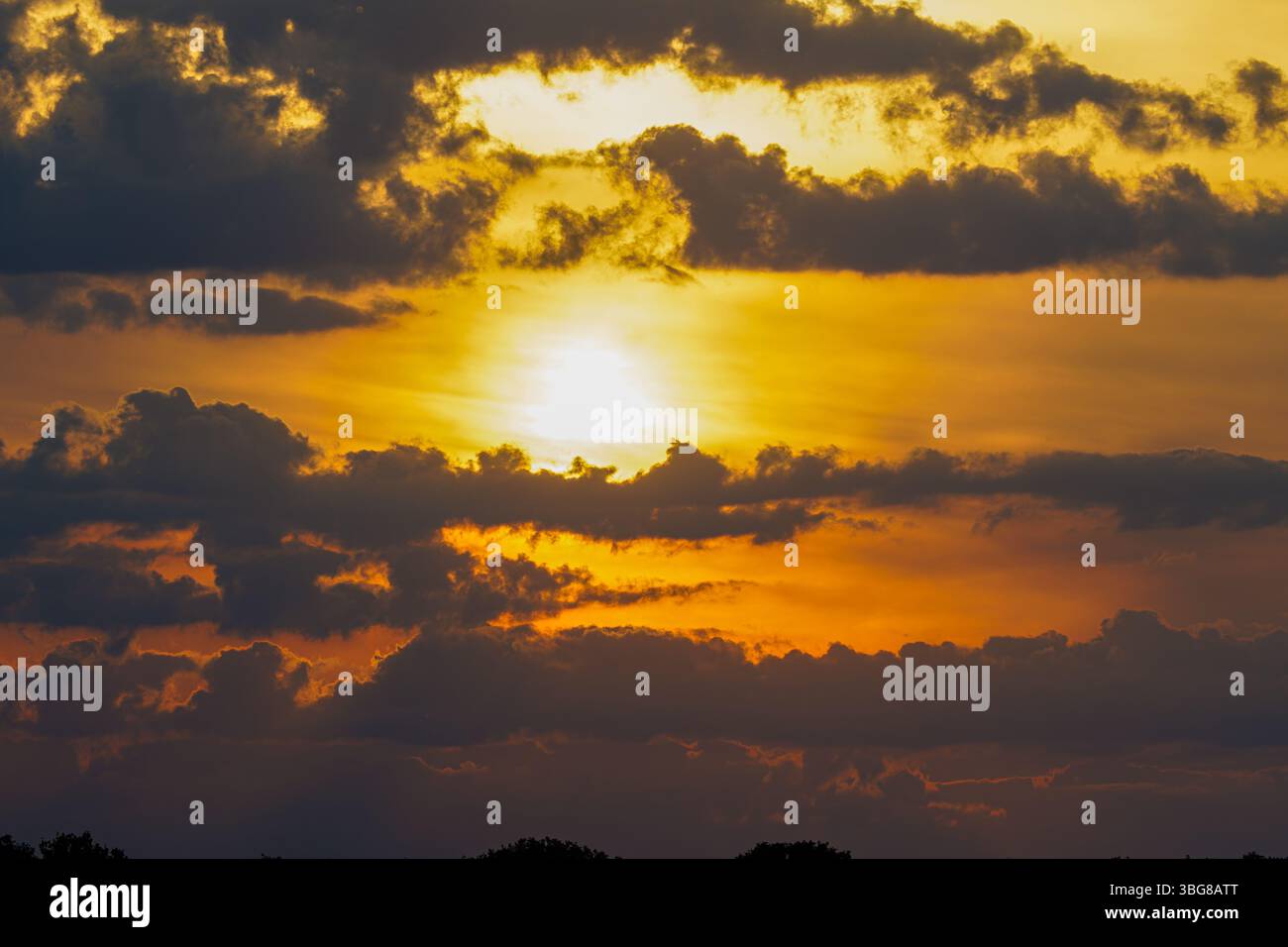 Un coucher de soleil spectaculaire aux teintes orange et jaune vibrantes, partiellement obscurcies par des nuages sombres, créant un contraste saisissant dans le ciel. Banque D'Images