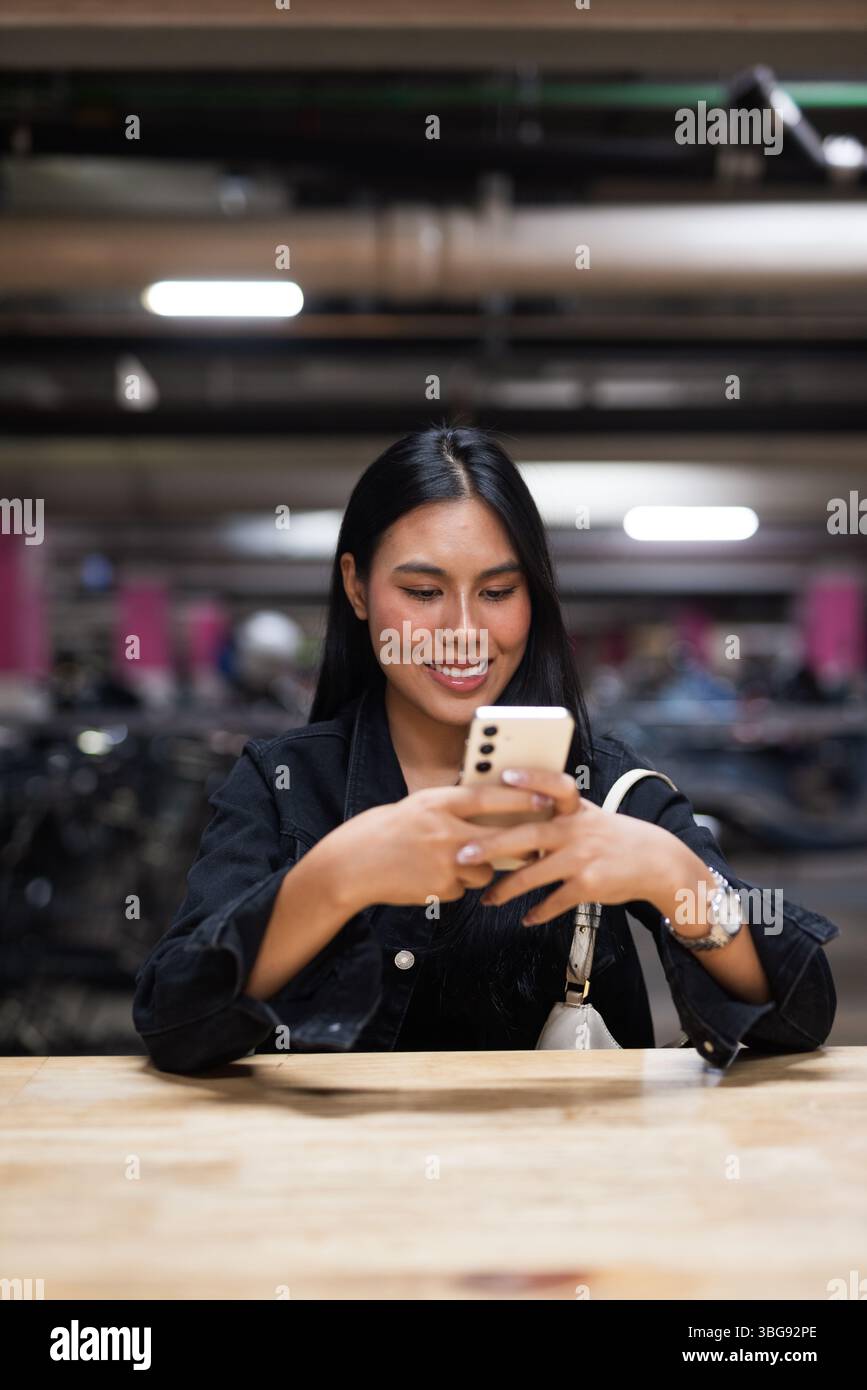 Portrait de jeune belle femme asiatique heureuse assise au parking pendant la nuit Banque D'Images