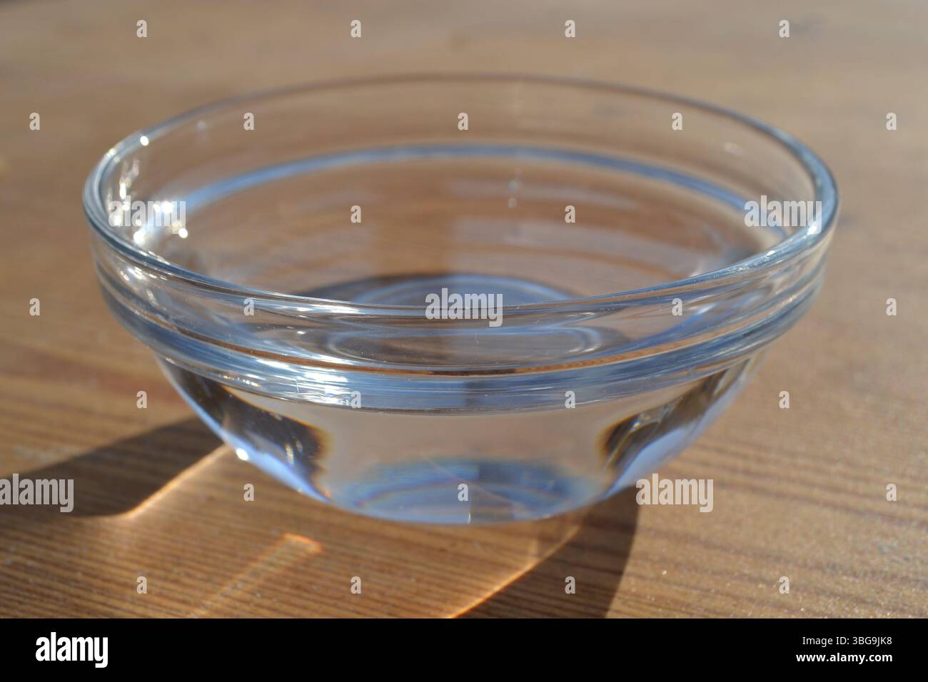 Vue latérale du bol transparent en verre vide comme une tasse sous la lumière du soleil avec son ombre sur fond de table en bois rayé brun. Restauration à boire. Banque D'Images