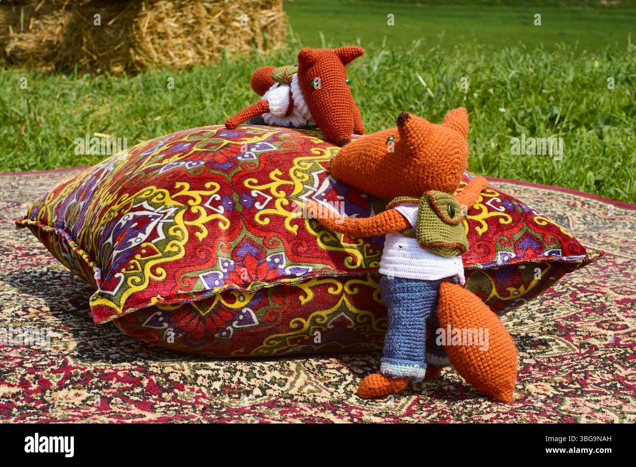 Deux jouets de renard en tricot doux, habillés de vêtements et avec des sacs à dos, blottis l'un à l'autre sur un tapis oriental coloré à côté d'un oreiller de jet, créant Banque D'Images