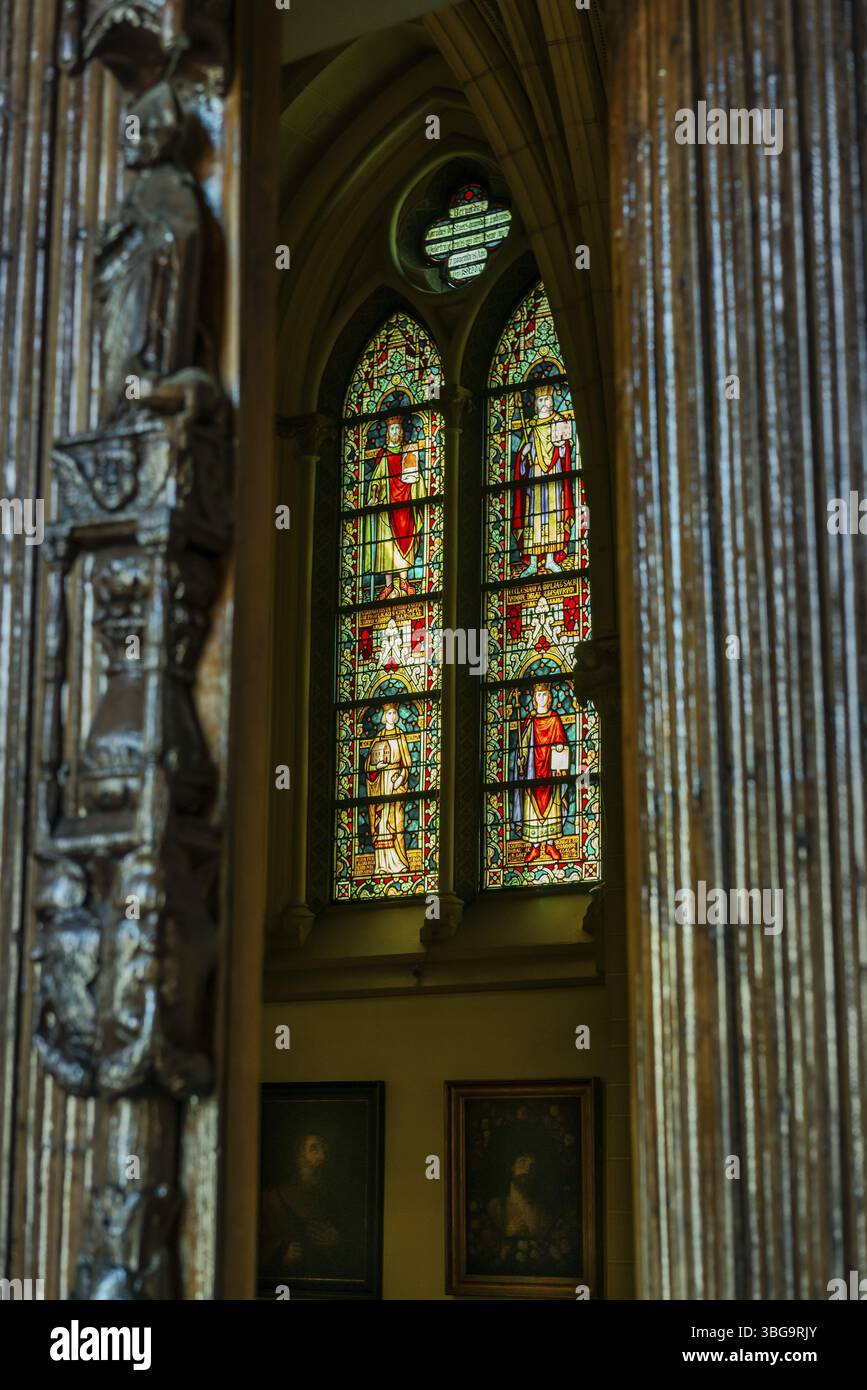 Une vue à travers un pilier en bois sculpté sur un vitrail lumineux dans une église Banque D'Images