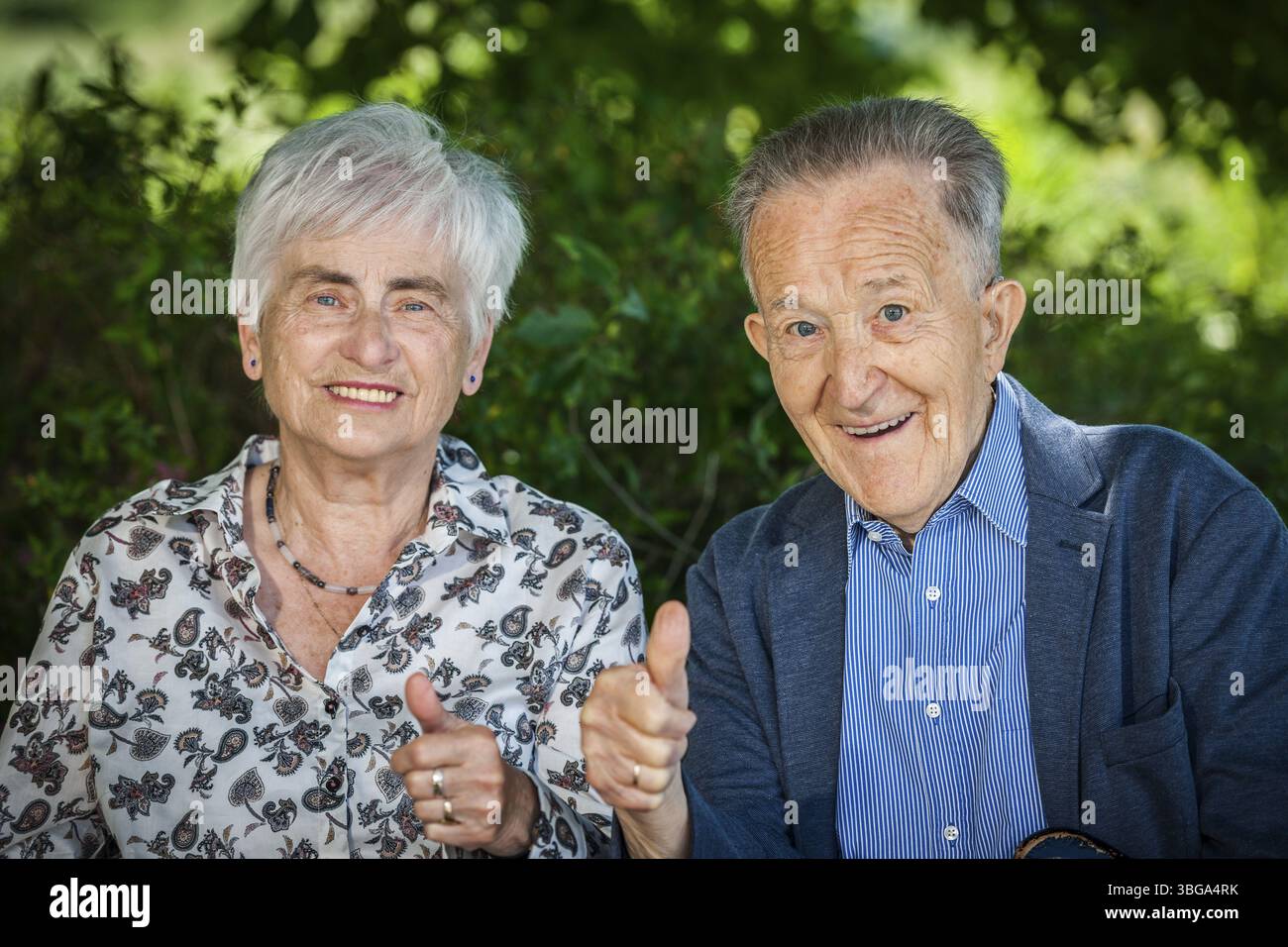 Portrait tête-et-épaule d'un couple retraité de 80 ans avant du fond vert des plantes montrant les pouces vers le haut et sympa en regardant le venu Banque D'Images