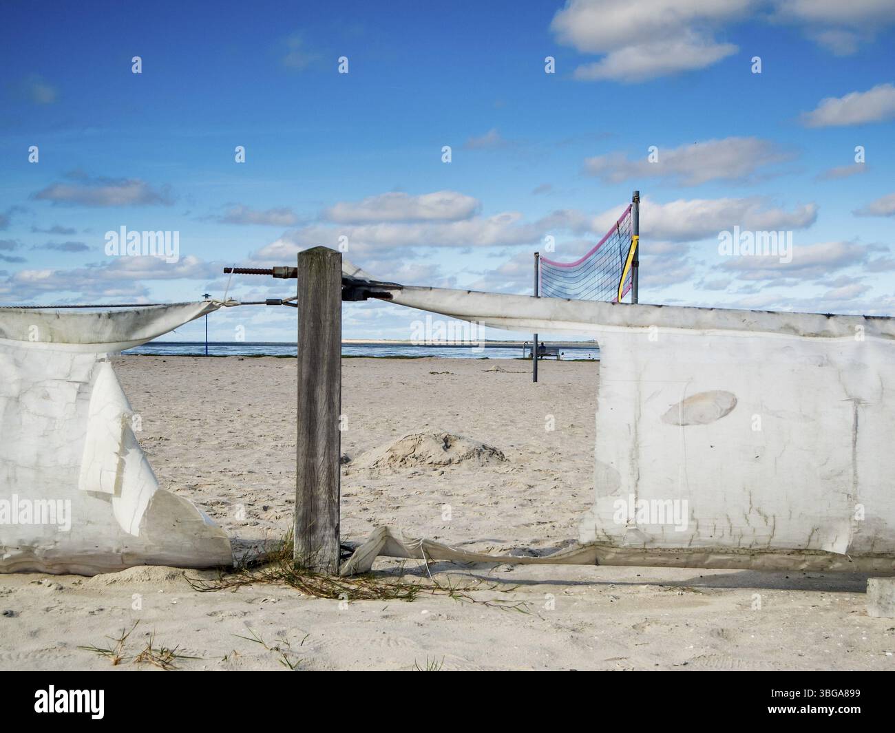 Scène sur la plage de Bensersiel dans le nord de l'Allemagne avec une clôture cassée devant un terrain de Beach volley devant un ciel bleu avec de petits nuages Banque D'Images