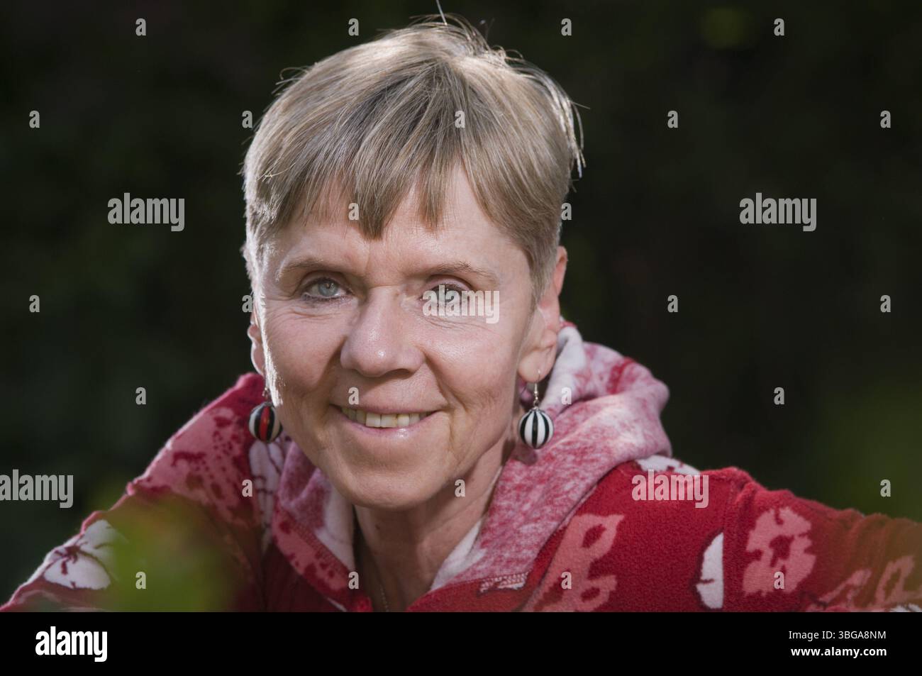 Portrait d'une femme âgée sur un banc de parc en été avec le haut du corps tourné vers l'arrière sur le dossier et regardant vers la caméra, Berlin, Banque D'Images