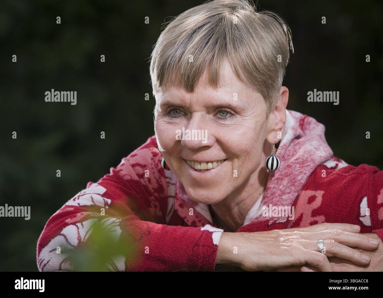 Portrait d'une femme âgée sur un banc de parc en été avec le haut du corps tourné vers l'arrière sur le dossier et regardant vers la caméra, Berlin, Banque D'Images