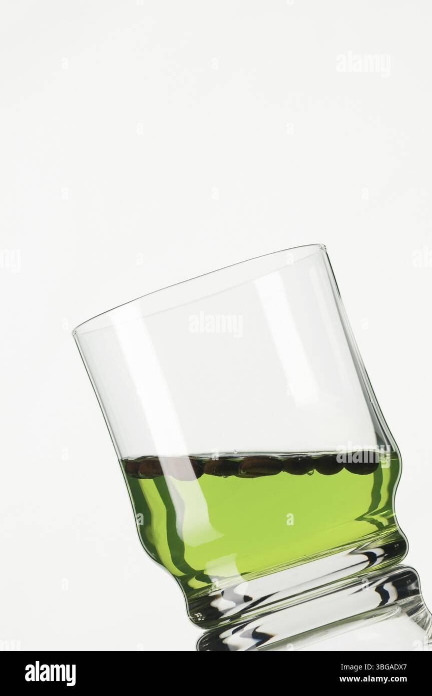Gros plan d'un verre rempli de liquide vert en angle sur fond blanc Banque D'Images