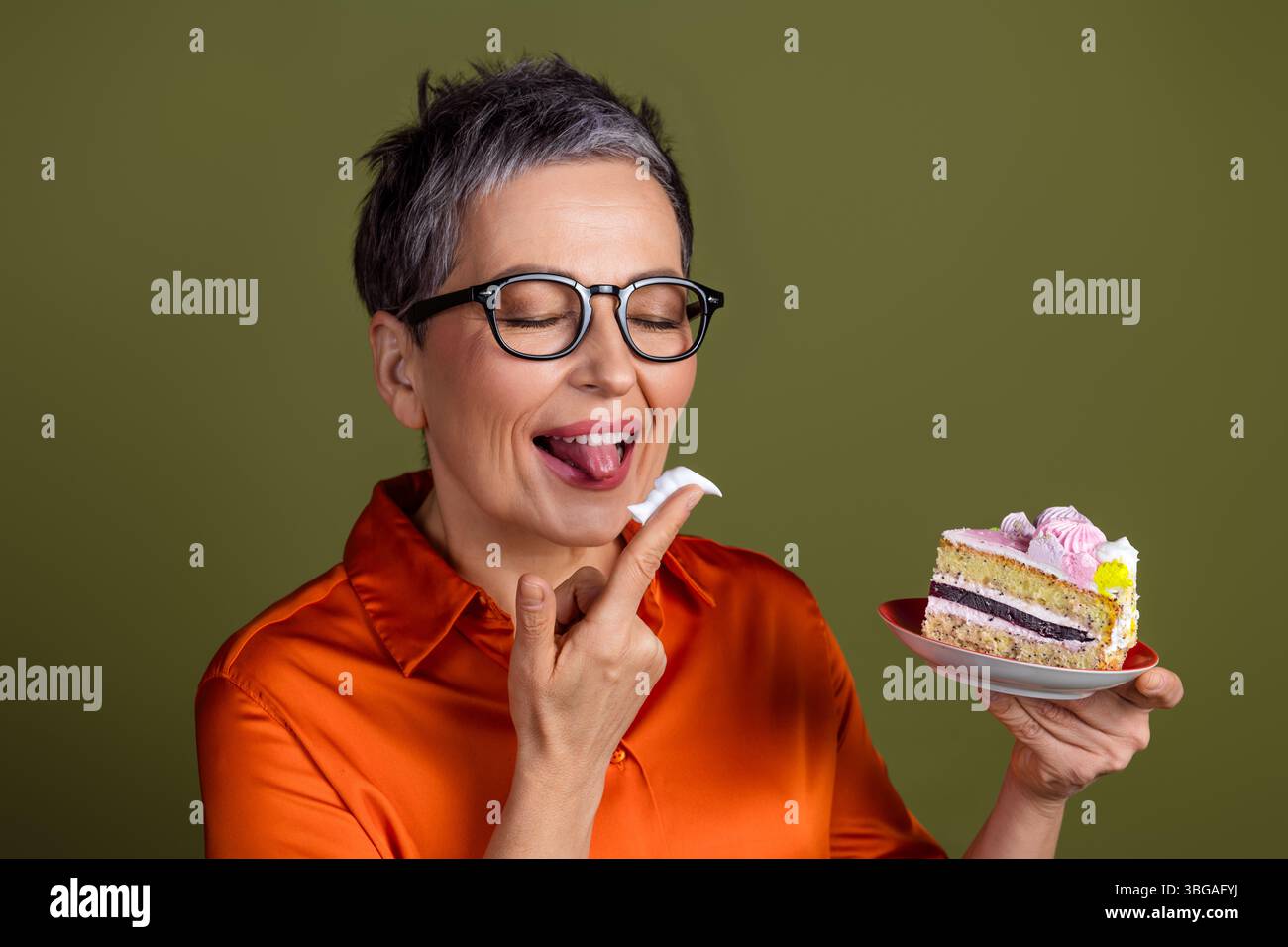 Femme mature dans une tenue élégante apprécie une tranche de gâteau avec enthousiasme et expression, sur un fond neutre Banque D'Images