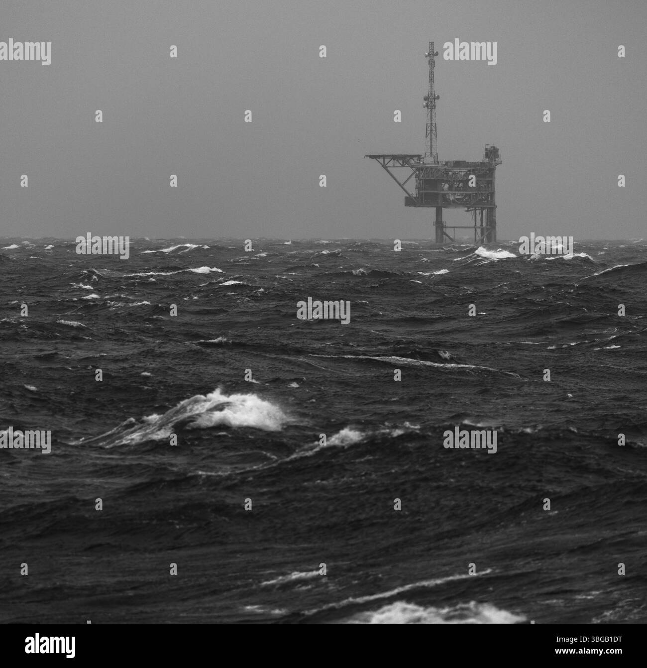 Une plate-forme pétrolière ou gazière offshore éloignée se tient seule dans des mers orageuses sous un ciel gris, capturée en noir et blanc par temps maritime intense Banque D'Images