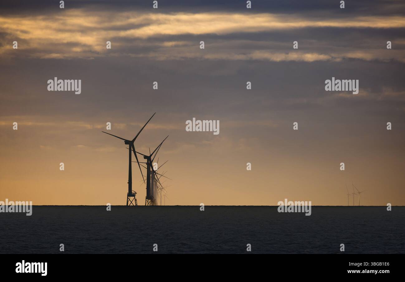 Des éoliennes offshore se silhouettent contre un ciel de coucher de soleil orange dans la mer du Nord. Infrastructures d'énergie renouvelable en eaux calmes. Banque D'Images
