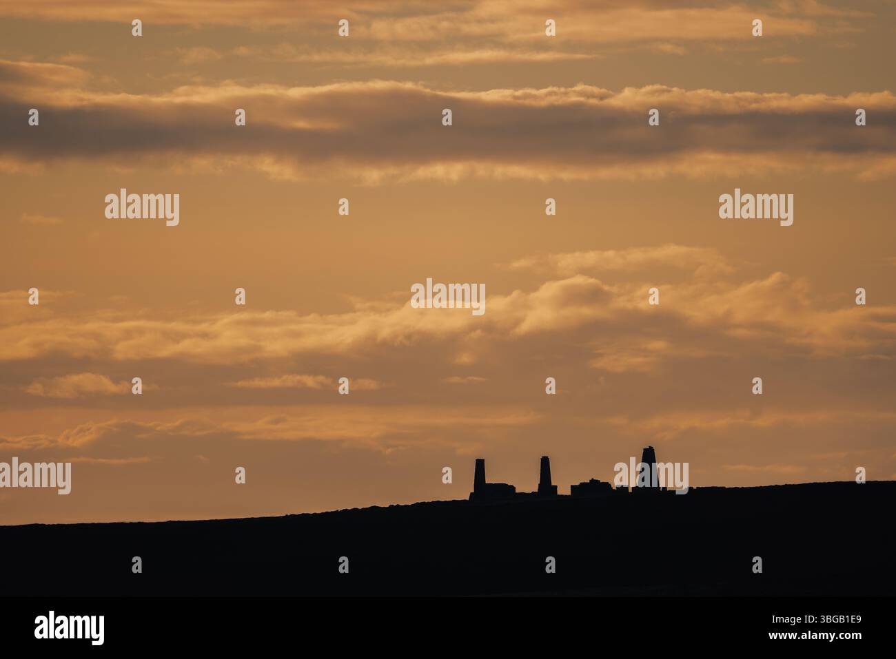 Ruines industrielles silhouettées sur les îles Orcades, en Écosse, contre un ciel de coucher de soleil doré atmosphérique. Capturé dans la lumière du début de soirée. Banque D'Images