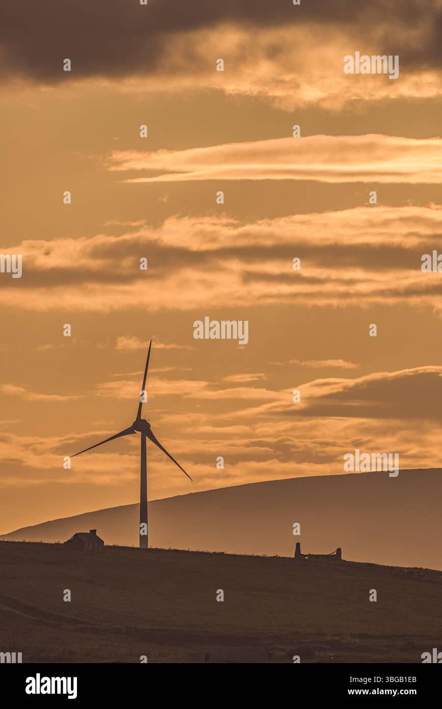 Une éolienne se dessinait contre un ciel doré près de ruines côtières sur les îles Orcades, en Écosse. Capturé au coucher du soleil. Banque D'Images