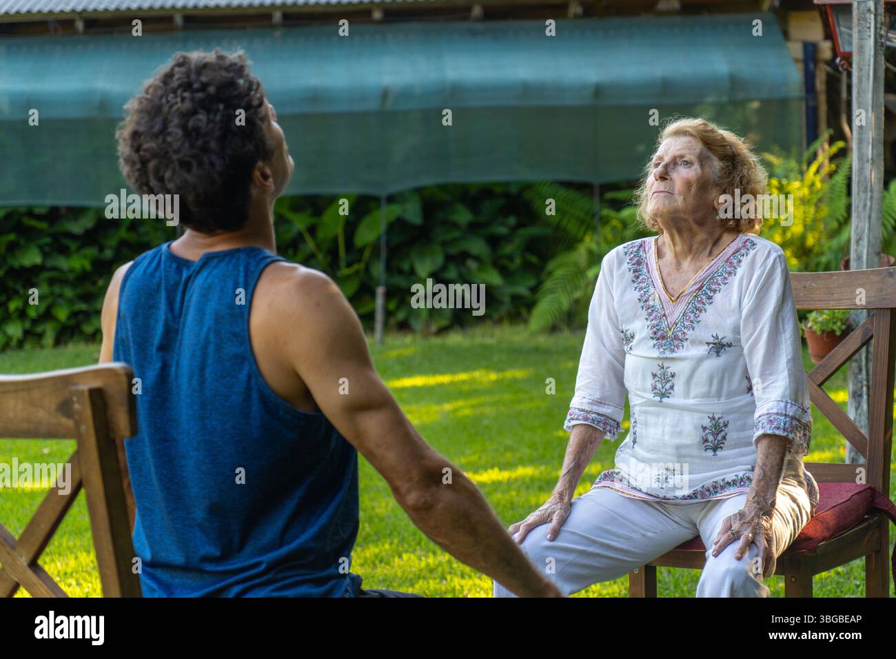 Une femme âgée et son physiothérapeute sont assis sur des chaises dans un jardin, pratiquant des exercices de respiration ensemble, en se concentrant sur l'amélioration de la hée respiratoire Banque D'Images
