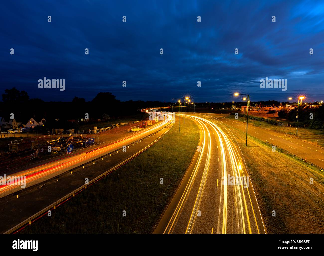 Longue exposition des voitures circulant sur l'autoroute au crépuscule, créant des traînées légères sous un ciel nuageux Banque D'Images