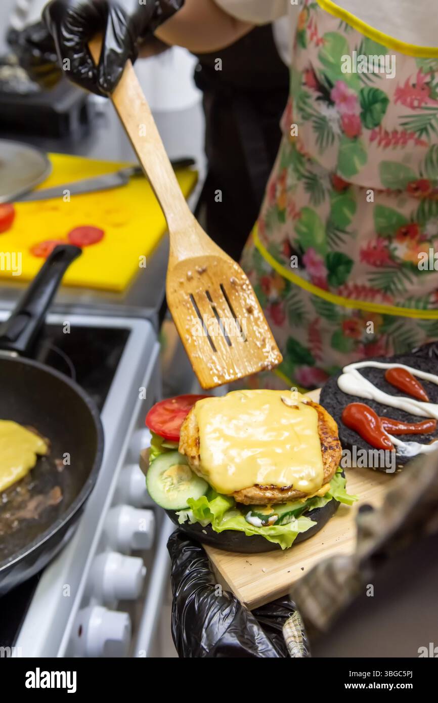 Masterclass colorée dans un café. les adolescents assemblent avec enthousiasme des hamburgers avec des petits pains noirs, des galettes et des légumes. Rires, travail d'équipe et délicieux résultats Grea Banque D'Images