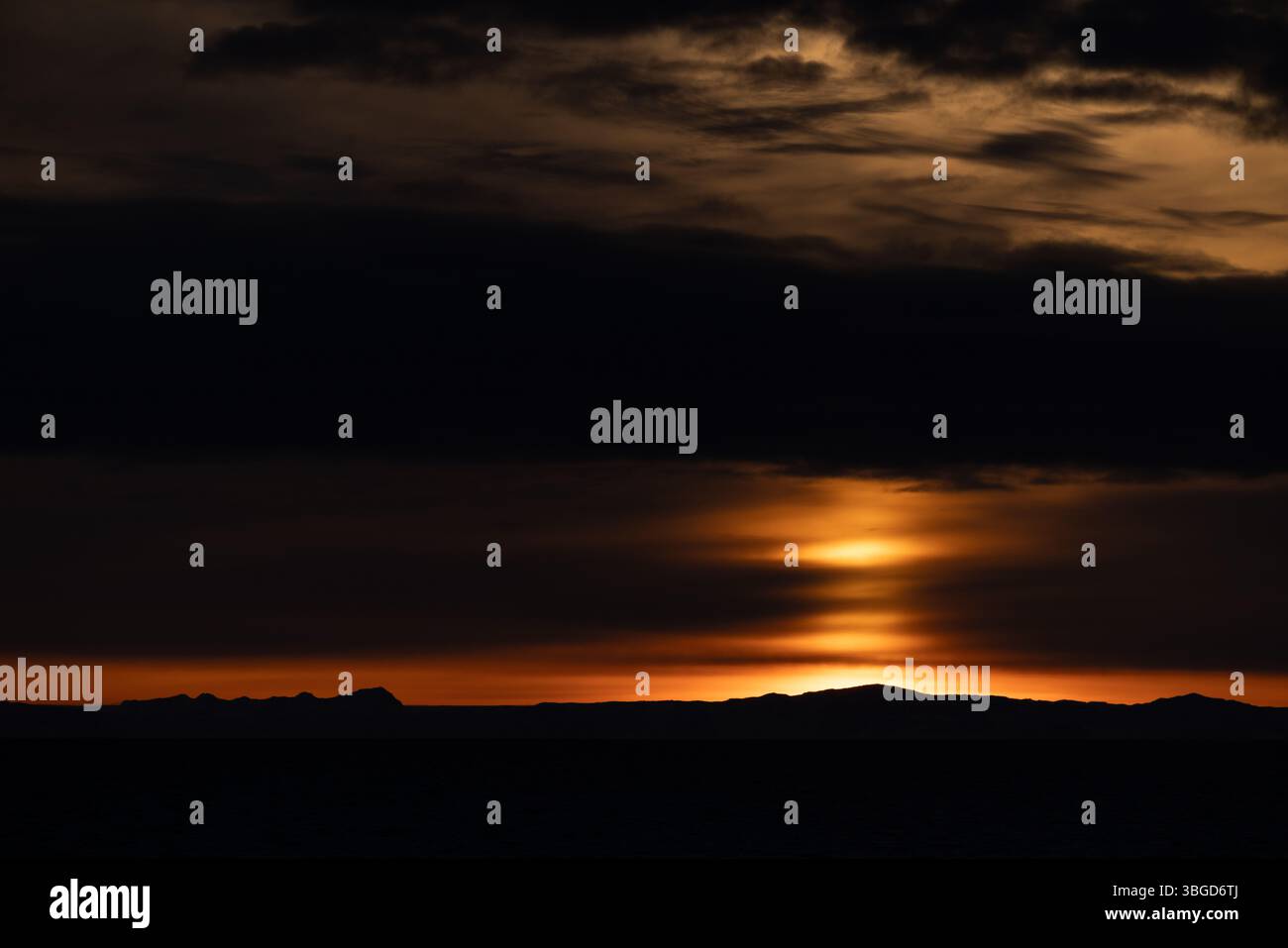 Coucher de soleil spectaculaire sur la côte silhouette dans le détroit de Davis, au Groenland, avec des nuages en couches et une lueur orange dans le ciel arctique. Banque D'Images