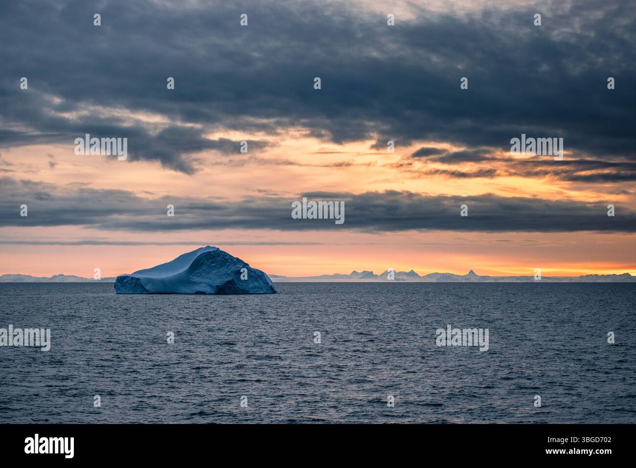 Un grand iceberg flotte sous un ciel nuageux dans le détroit de Davis, avec des sommets lointains recouverts de neige du Groenland éclairés par le doux crépuscule arctique. Banque D'Images