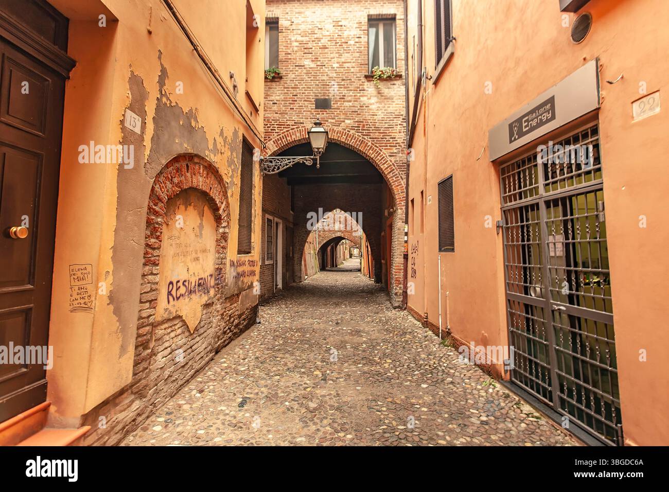 Ferrare, Italie 2 janvier 2025 : ruelle étroite avec rue pavée et succession d'arcades en briques à ferrare, italie Banque D'Images