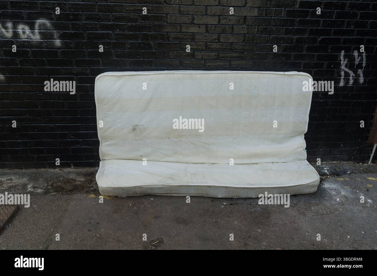 Un matelas s'est déversé dans une ruelle latérale contre un mur de briques noires en grande-bretagne Banque D'Images