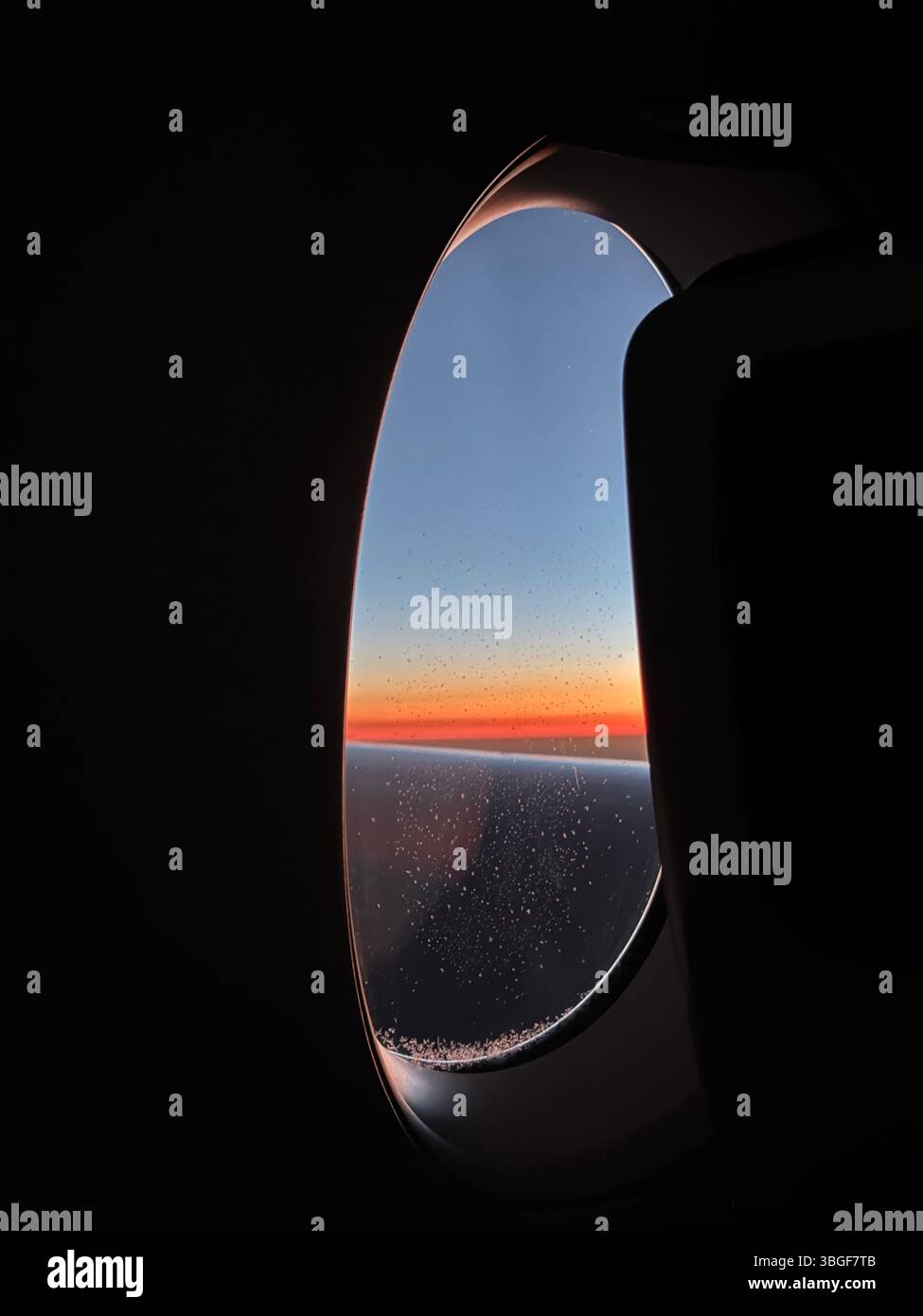 Vue de la fenêtre de l'avion au coucher du soleil, montrant des gradients orange et bleu vifs au-dessus de l'horizon en vol. Banque D'Images