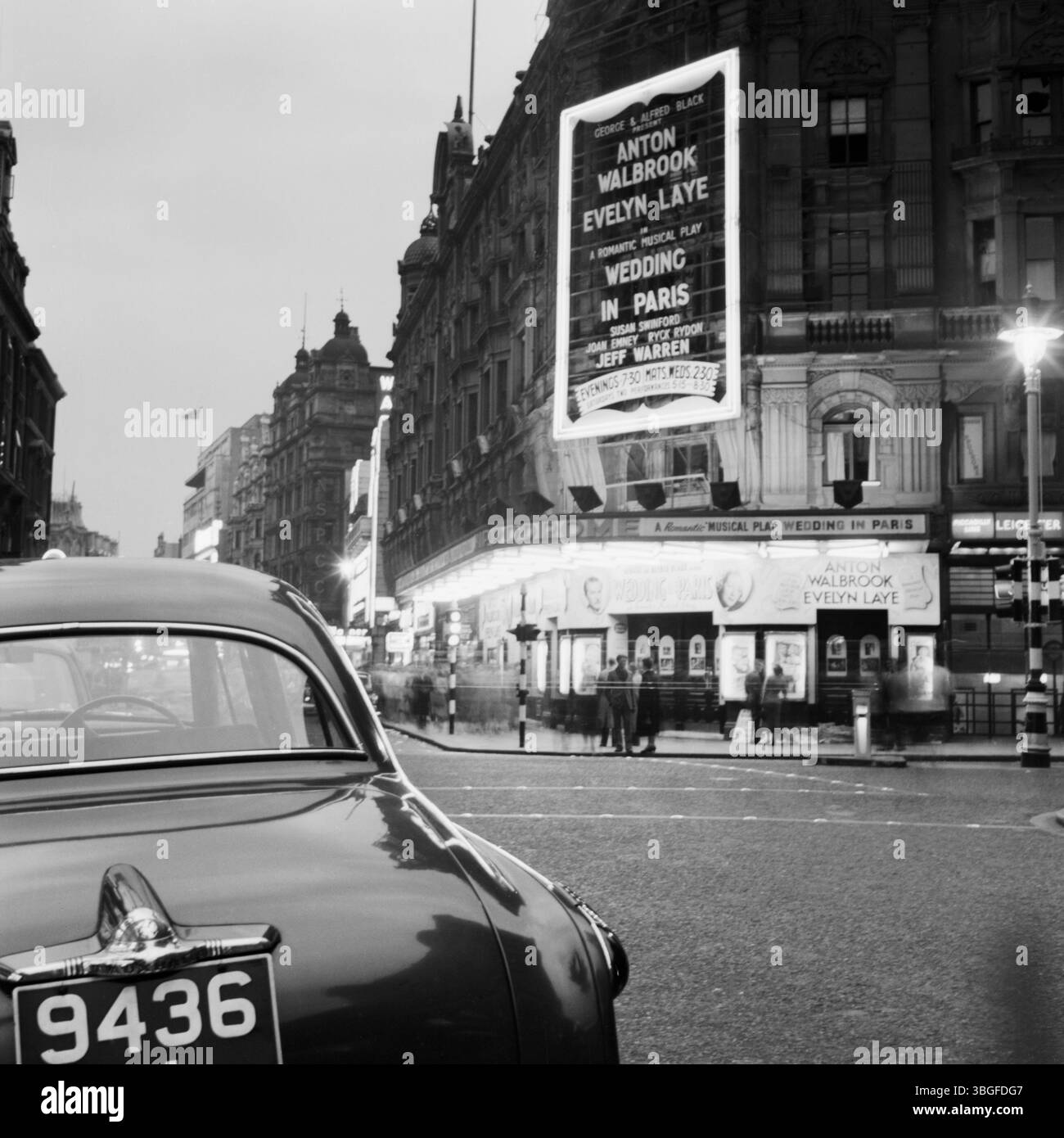 Abendliche Straßenszene in London vor dem beleuchteten London Pavilion am Piccadilly Circus, WO das musical Wedding in Paris mit Anton Walbrook und Evelyn Laye gezeigt wird. IM Vordergrund ist ein parkendes auto mit britischem Nummernschild zu sehen, Aufnahme von 1954. Banque D'Images