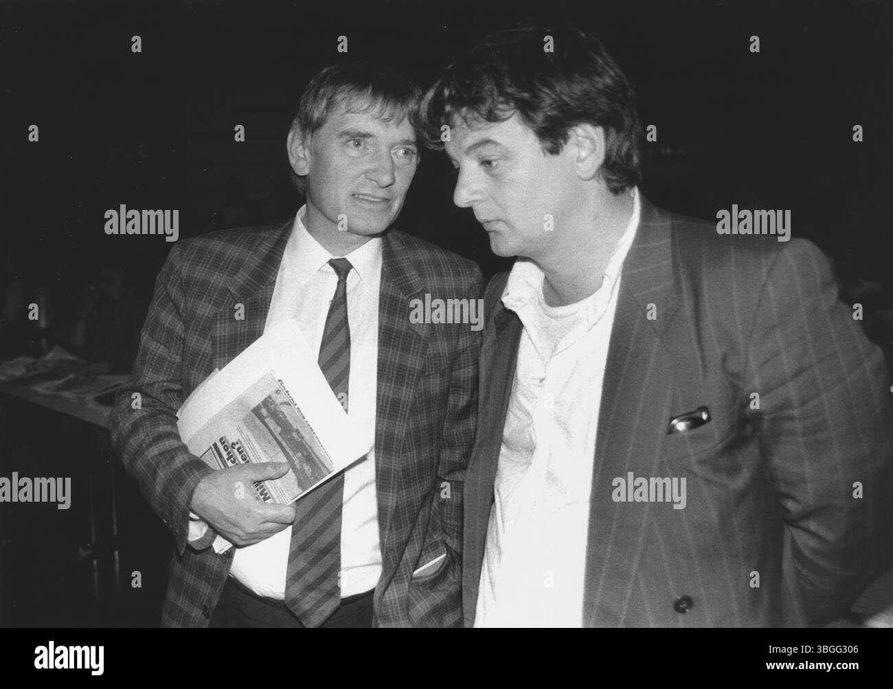 Joschka Fischer (rechts) im Gespräch mit Otto Schily (links) auf der Bundesversammlung der Grünen am 27. Septembre 1986. Beide Politiker stehen in enger Nähe, vertieft in eine ernste Unterhaltung. Fischer trägt ein weit geöffnetes Hemd unter einem gestreiften Sakko, während Schily mit klassischem Hemd, Krawatte und karierter Jacke das Kontrastbild eines bürgerlichen Politikers abgibt – eine stilistische Metapher für die Spannungsfelder innerhalb der Partei in jener Zeit. Banque D'Images