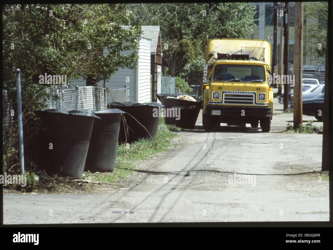 Un camion à ordures jaune de la ville de Columbus descend une ruelle en 1980, ramassant de grandes poubelles dans le cadre du projet pilote pour un système de collecte des déchets entièrement automatisé. Le système a été mis en œuvre pour la première fois en 1984. Banque D'Images