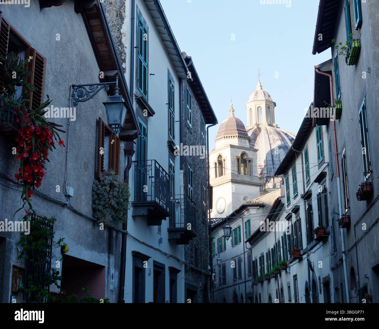 Rue historique étroite avec des fleurs suspendues aux fenêtres et le dôme de la cathédrale de Montefiascone derrière, région du Latium, Italie. 3 juin 2025 Banque D'Images