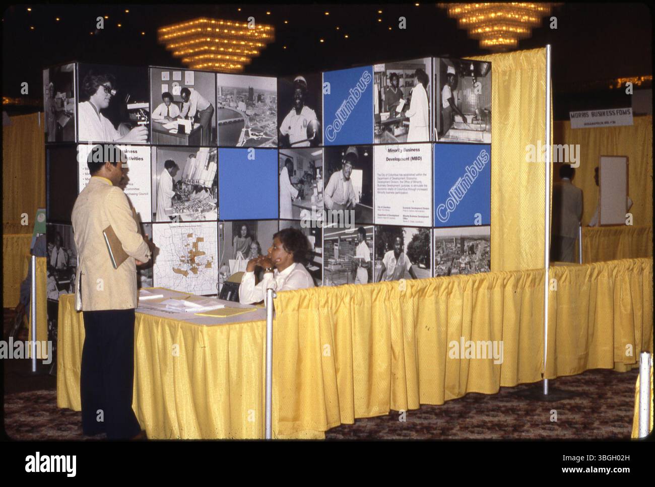 Une femme au stand Columbus Minority Business Development au Forum '80, une conférence commerciale tenue en 1980. Elle interagit avec un homme au stand, qui promeut le développement des affaires minoritaires au sein de Columbus, parrainé par la Division du développement économique de la ville. Banque D'Images