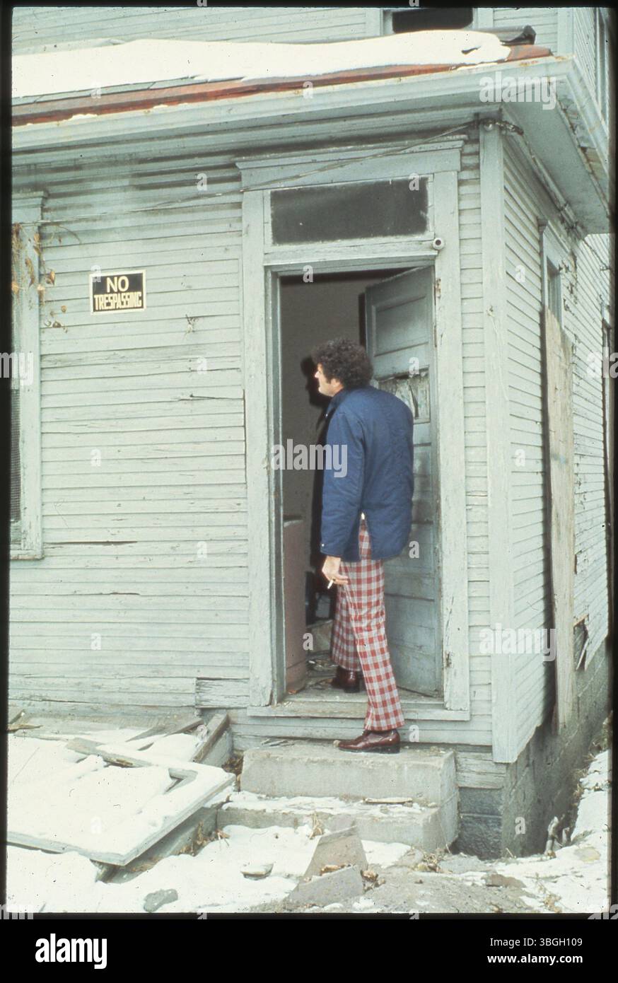 Un homme se tient devant la porte d'une maison abandonnée, avec un signe visible « interdiction d'intrusion » au premier plan. La maison semble délabrée et négligée. Banque D'Images