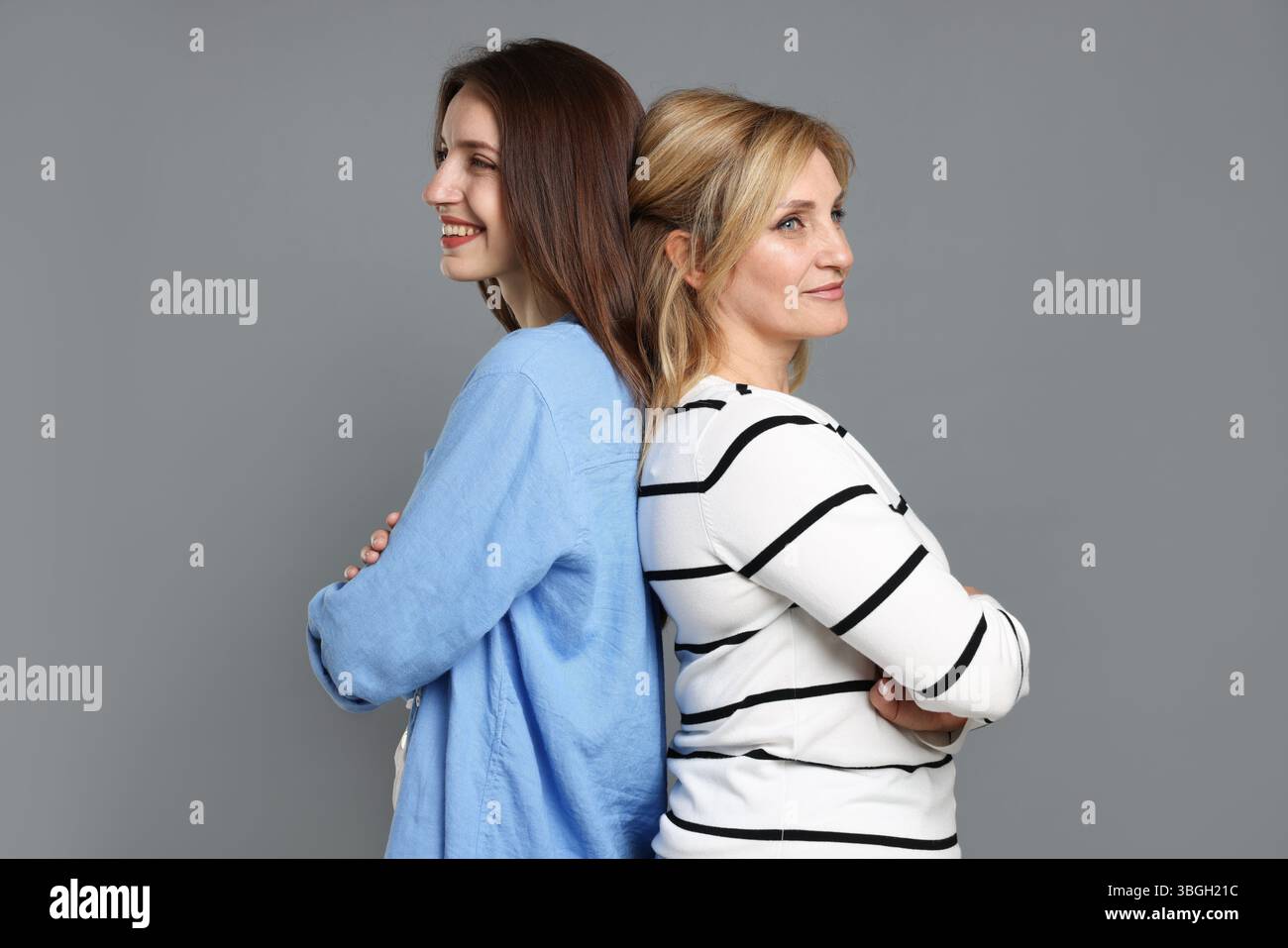Mère et fille joyeuses dos à dos sur fond gris Banque D'Images