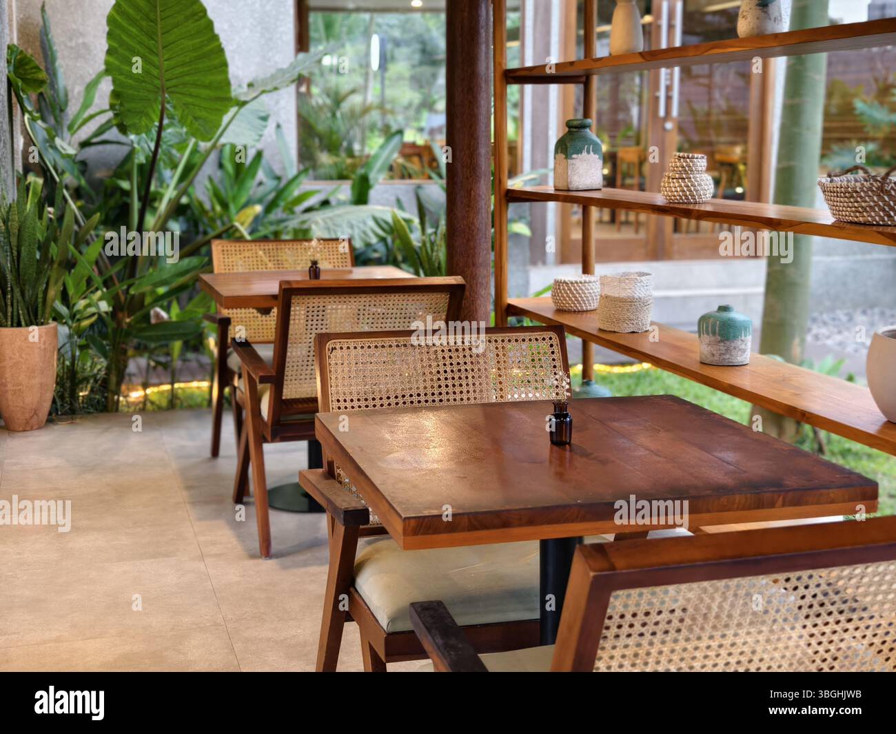Un coin salon de café inspiré de la nature avec des tables en bois, des chaises en rotin et des poteries décoratives sur des étagères en bois ouvertes Banque D'Images