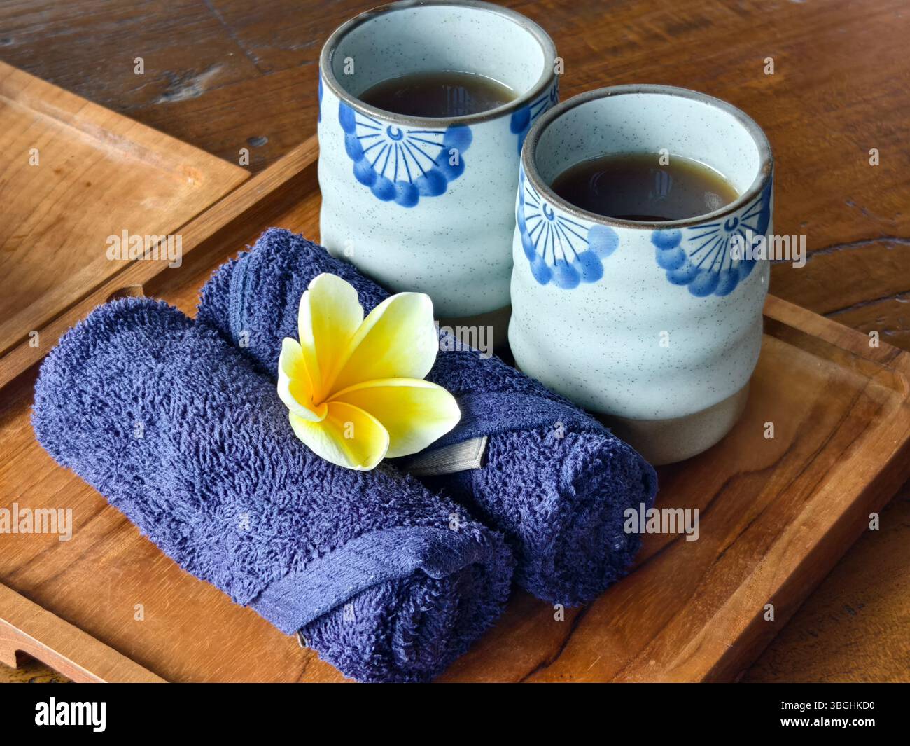 Un rituel de bienvenue apaisant avec tasses de tisane, serviettes chaudes et une fleur de frangipanier Banque D'Images