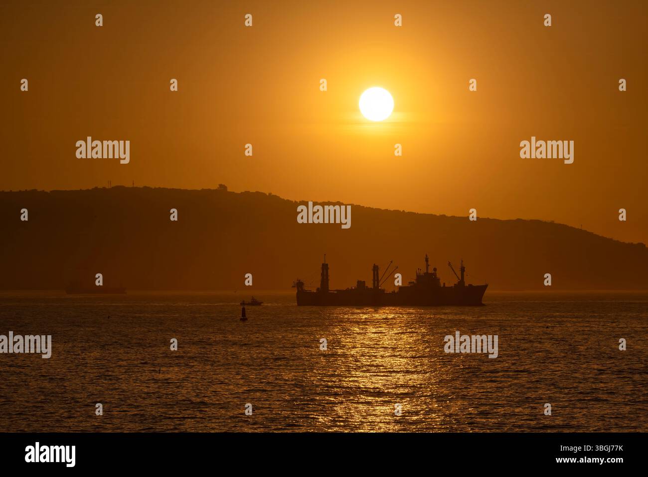 Un bateau de pêche navigue dans les eaux tranquilles de Valparaiso, au Chili, tandis que le soleil se couche derrière une colline lointaine, projetant une lueur dorée chaude à travers le port Banque D'Images