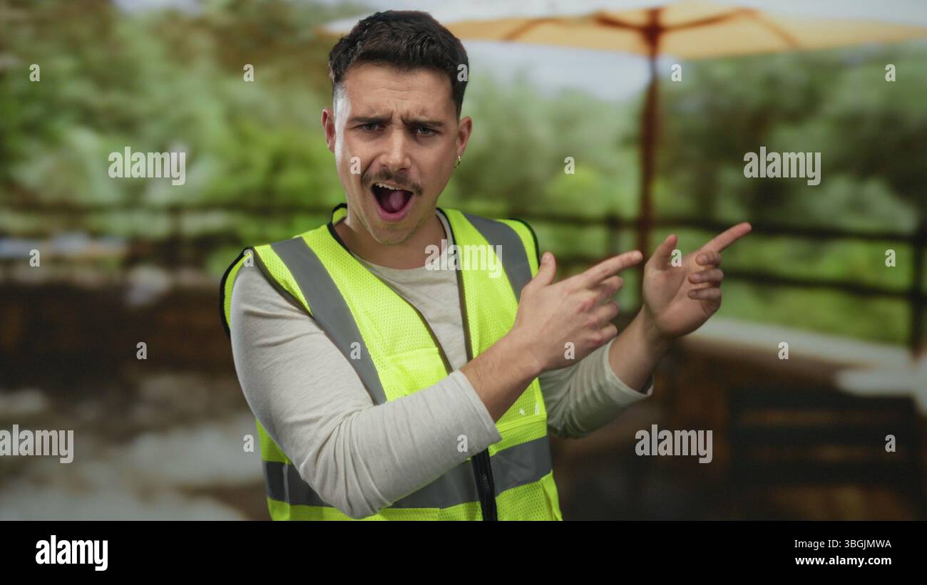 Jeune homme en pointes de gilet réfléchissant surpris dans un cadre de parc avec une verdure luxuriante sous un grand parapluie, évoquant la curiosité dans un environnement extérieur Banque D'Images