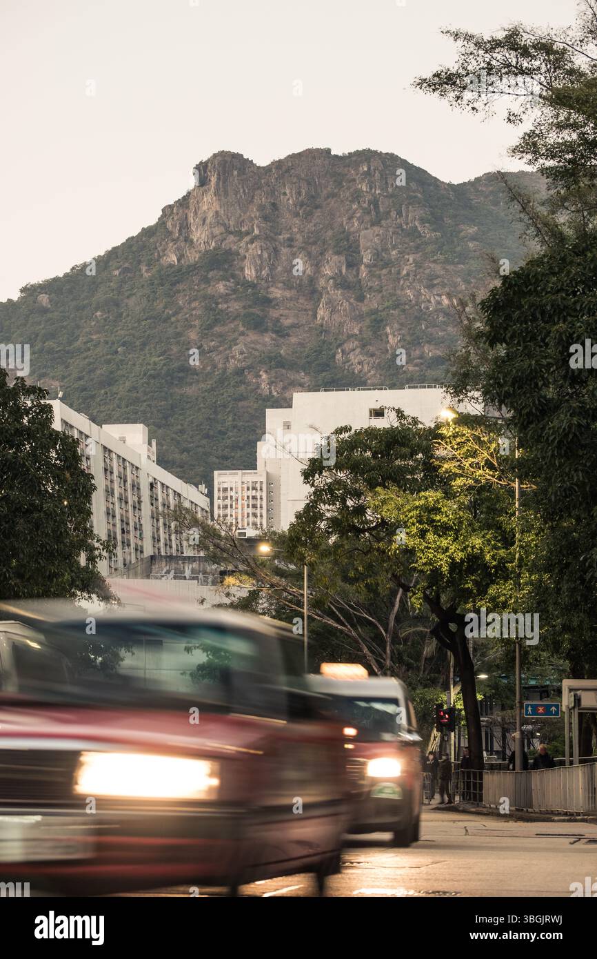 Scène de rue à Kowloon Tong, Hong Kong, avec un taxi en mouvement au premier plan et l'emblématique montagne Lion Rock en arrière-plan. Banque D'Images