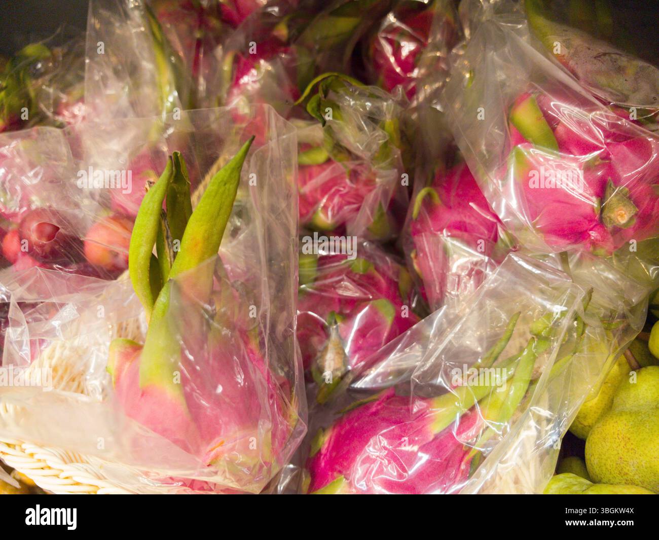 Les fruits du dragon rose vif sont soigneusement enveloppés dans du plastique, mettant en valeur leur forme et leurs couleurs uniques. Cette exposition sur un marché local animé invite Banque D'Images